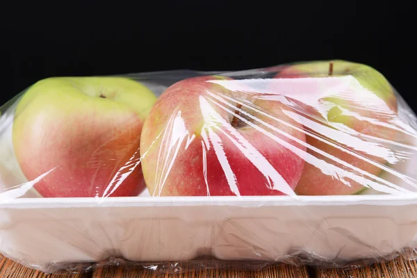 Яблоки упаковали вещи в продовольственном фильме на столе на черном фоне — стоковое фото