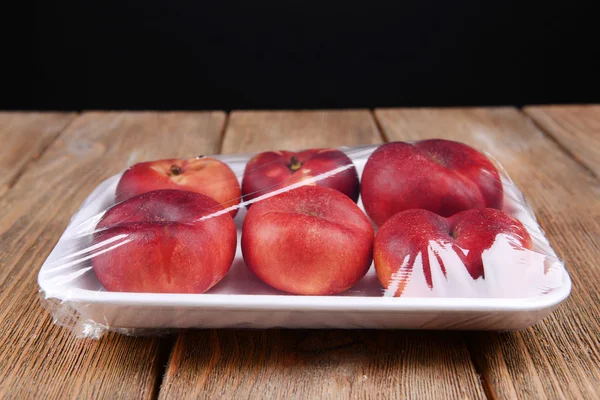 Персики в пищевой пленке на стол на черном фоне — стоковое фото
