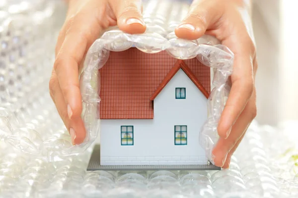 Руки женщина, охватывающих модель дома с пузырь обернуть дом защиты или страхования концепции — стоковое фото
